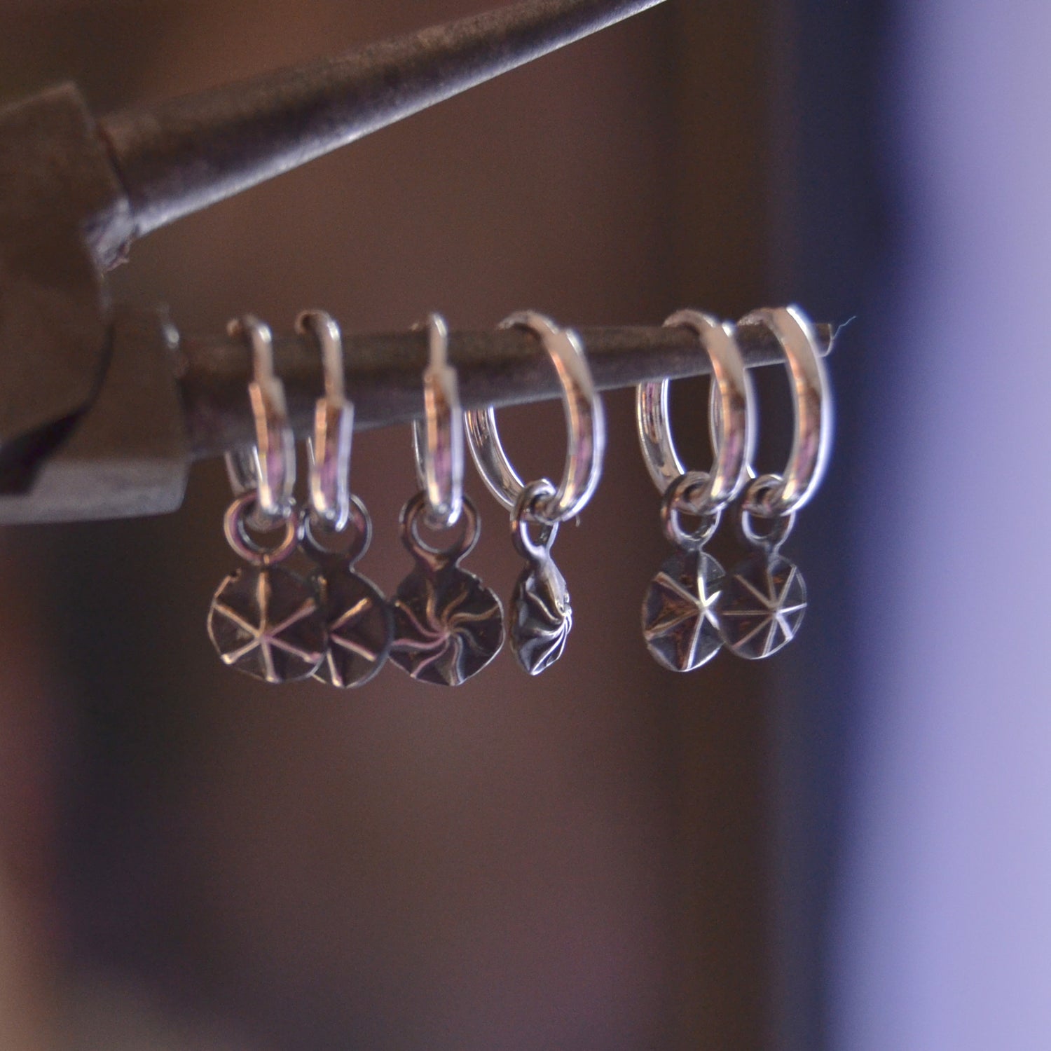 Close-up of handcrafted sterling silver hoop earrings with dangling star-etched charms. The earrings are displayed hanging on a rod, showcasing their polished finish and intricate celestial design.

