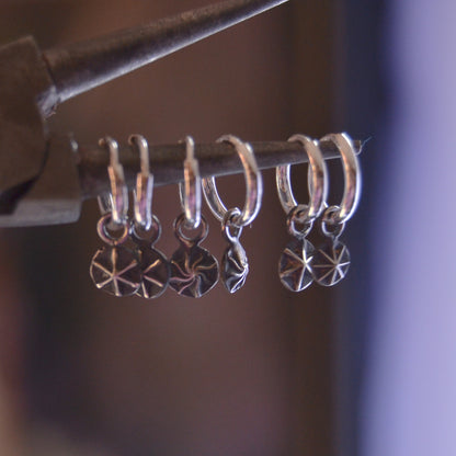 Close-up of handcrafted sterling silver hoop earrings with dangling star-etched charms. The earrings are displayed hanging on a rod, showcasing their polished finish and intricate celestial design.

